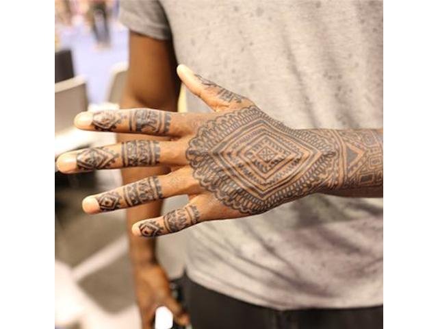 A detailed close-up of a dark botanical jagua tattoo on a person's forearm.