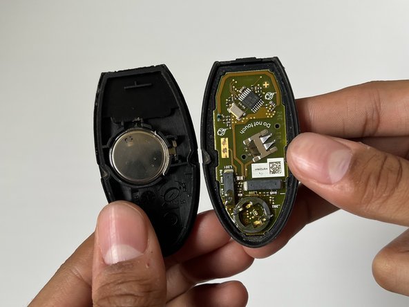 An Infiniti key fob on a workbench with a battery and precision screwdriver.